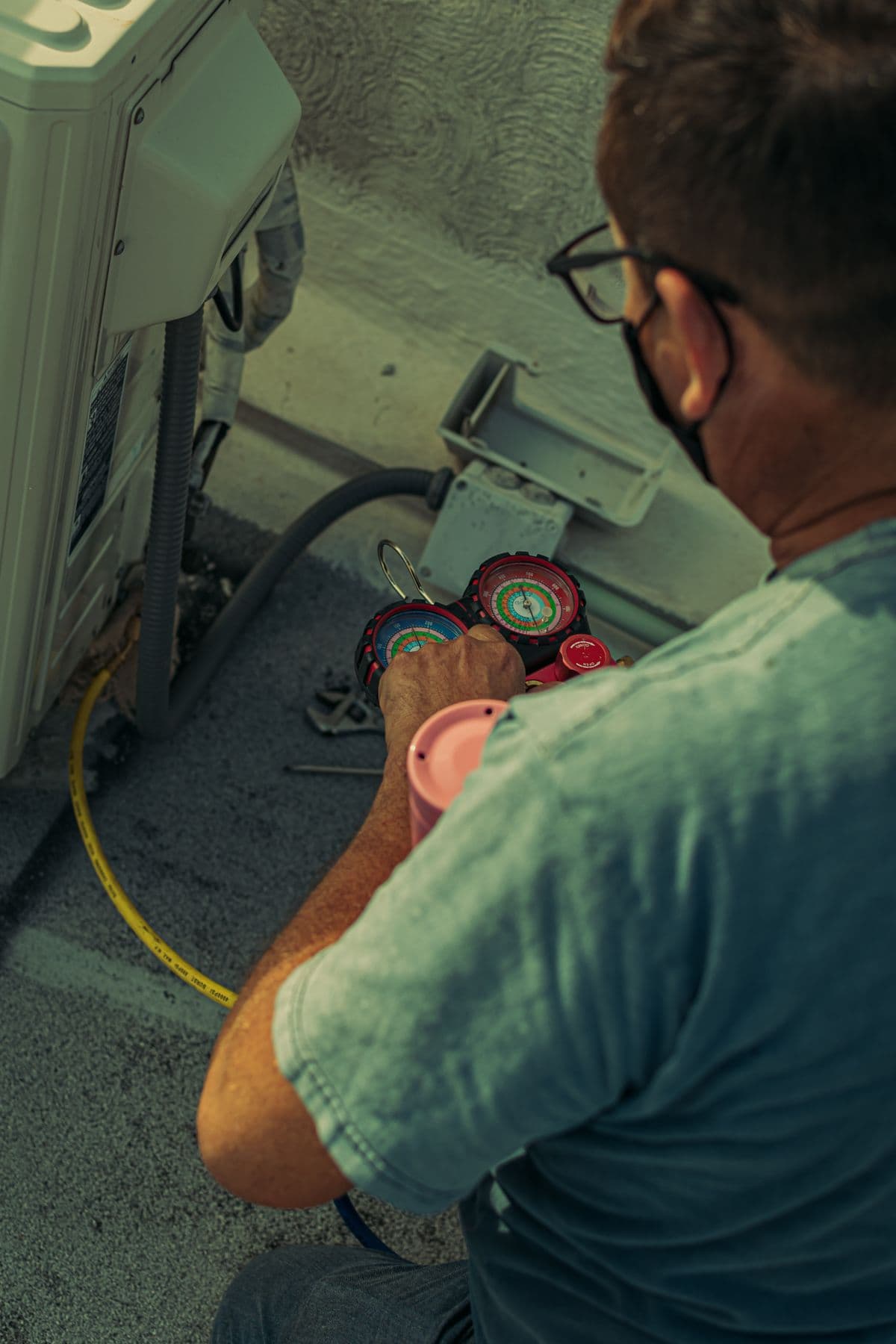 HVAC technician servicing an outdoor unit with manifold gauges